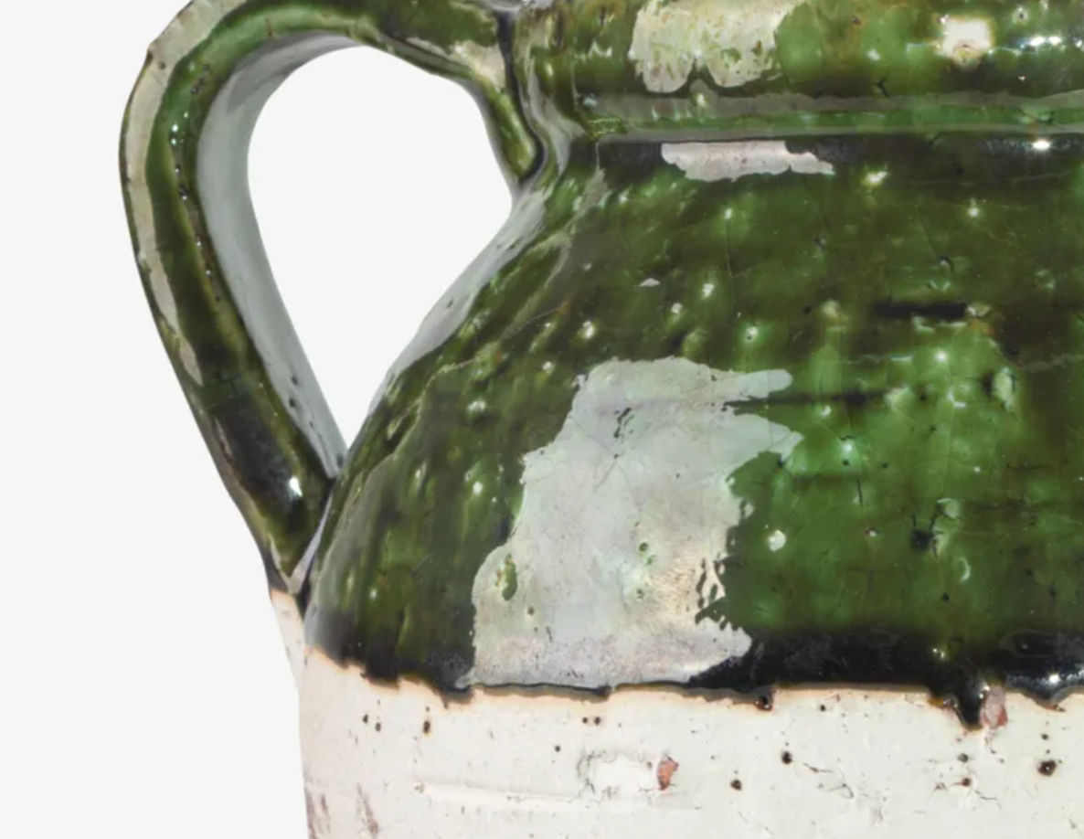 Close-up of a ceramic jug with a glossy dark green glaze and a distressed, unglazed white base, shown against a plain white background.